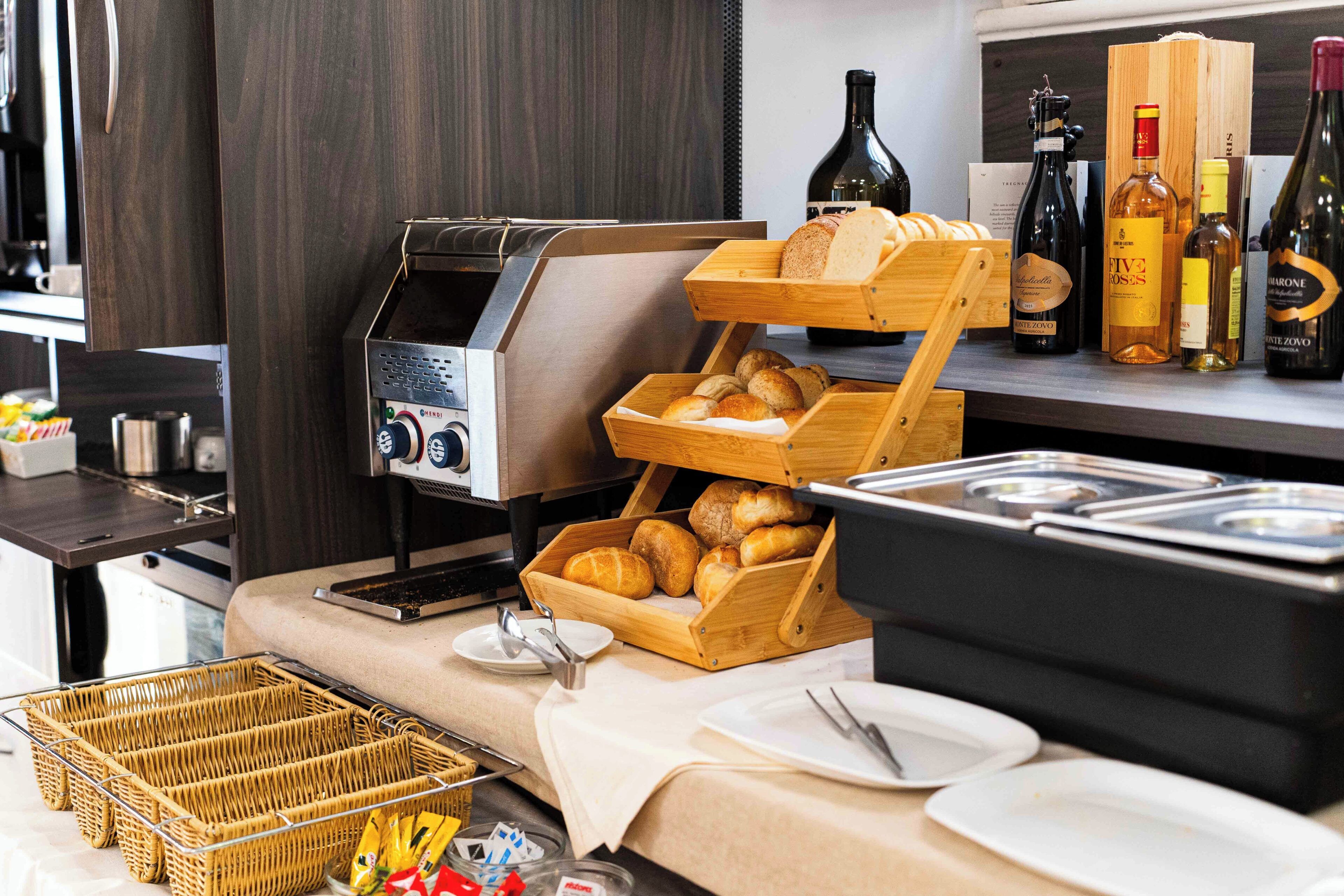 A breakfast buffet setup with bread, pastries, and wine bottles.