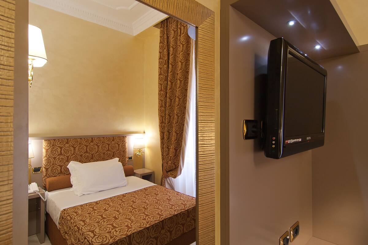 Ein Hotelzimmer mit einem Bett, einem an der Wand montierten Fernseher und einem Nachttisch mit Lampe.