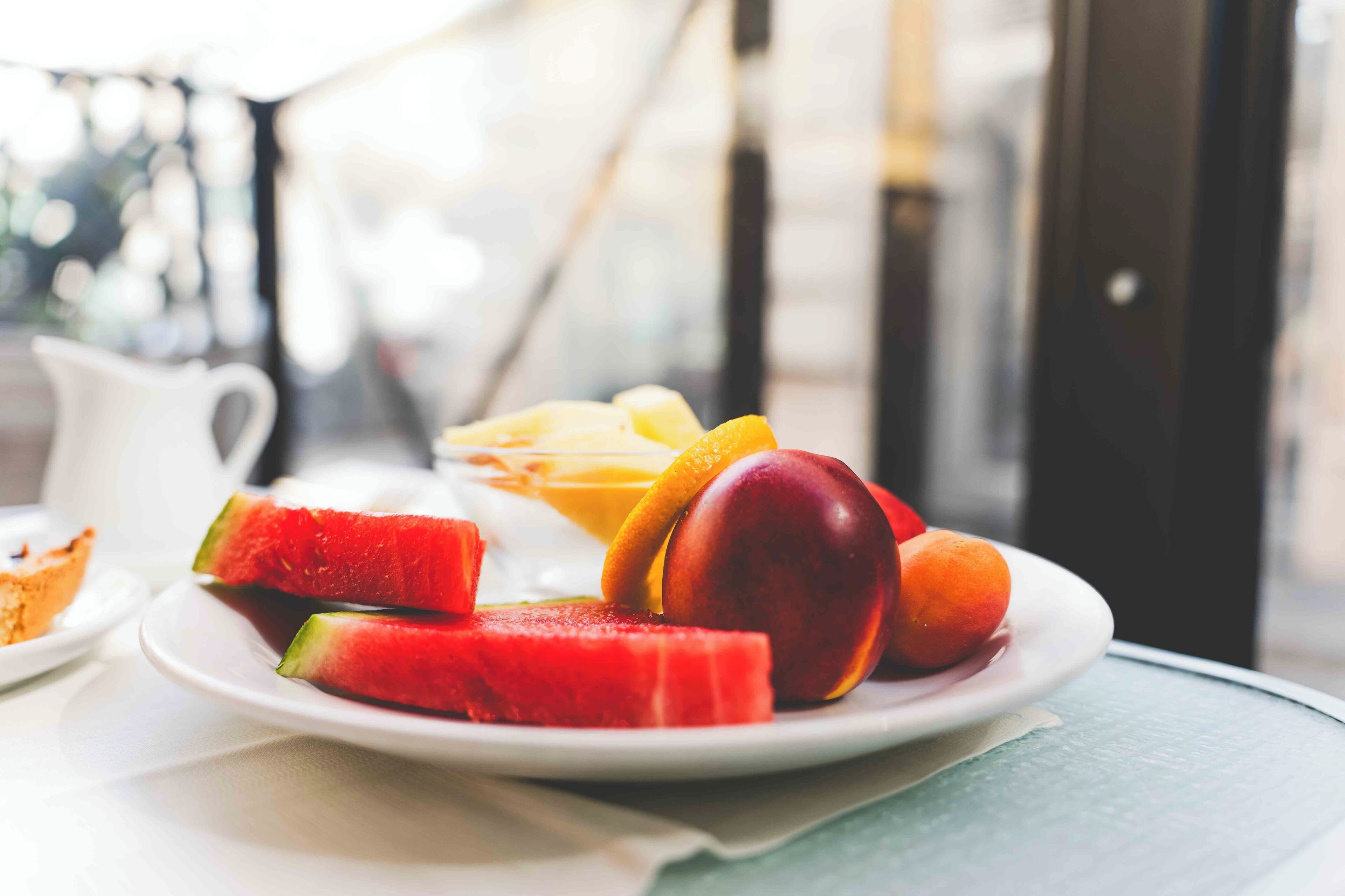 A plate with watermelon, peach, and orange slices on a table.