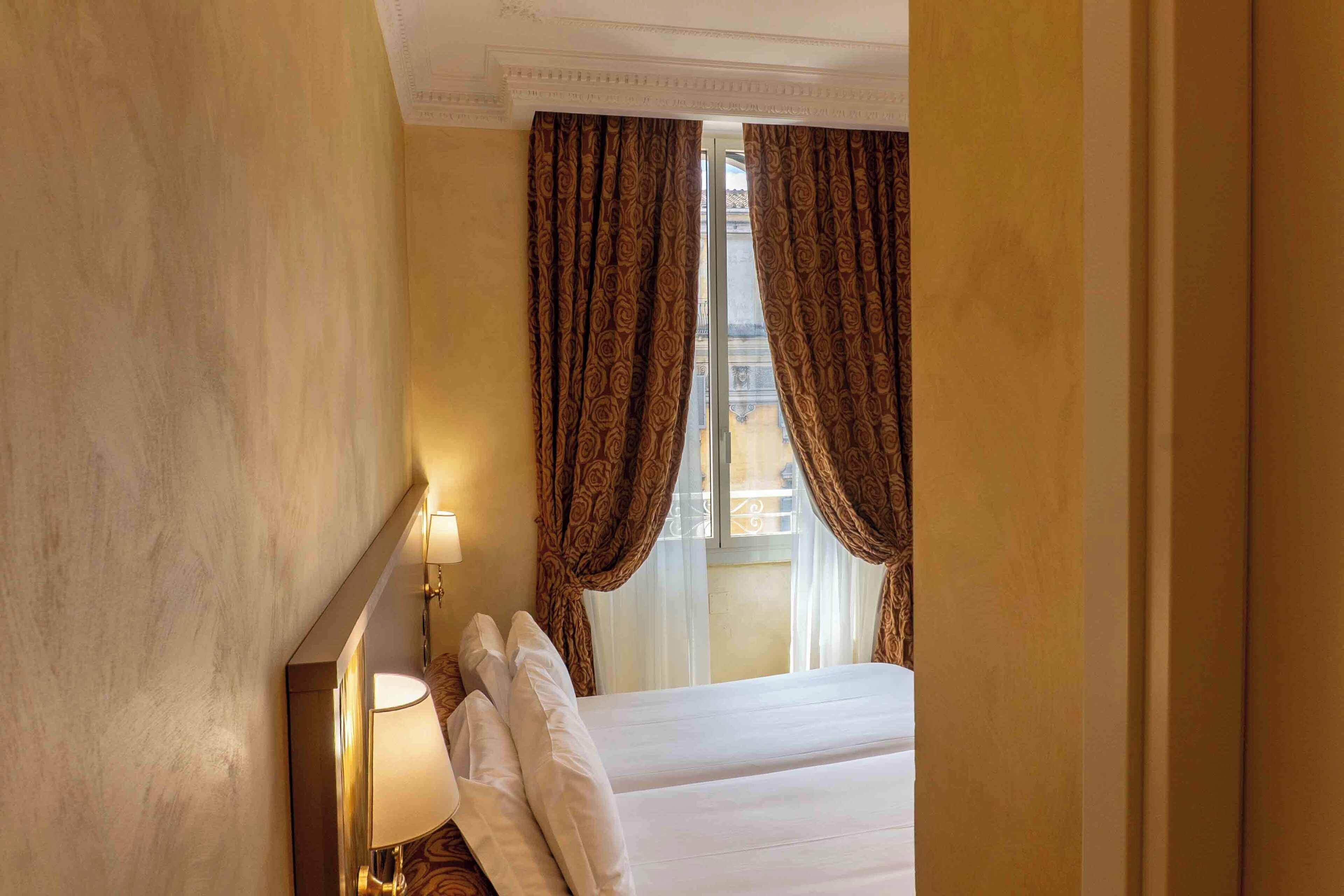 A hotel room with a bed, a nightstand with a lamp, and a window with curtains.