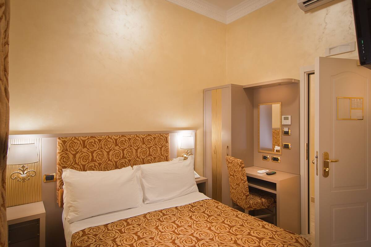 Ein Hotelzimmer mit Bett, Schreibtisch, Stuhl, Spiegel und Kleiderschrank.