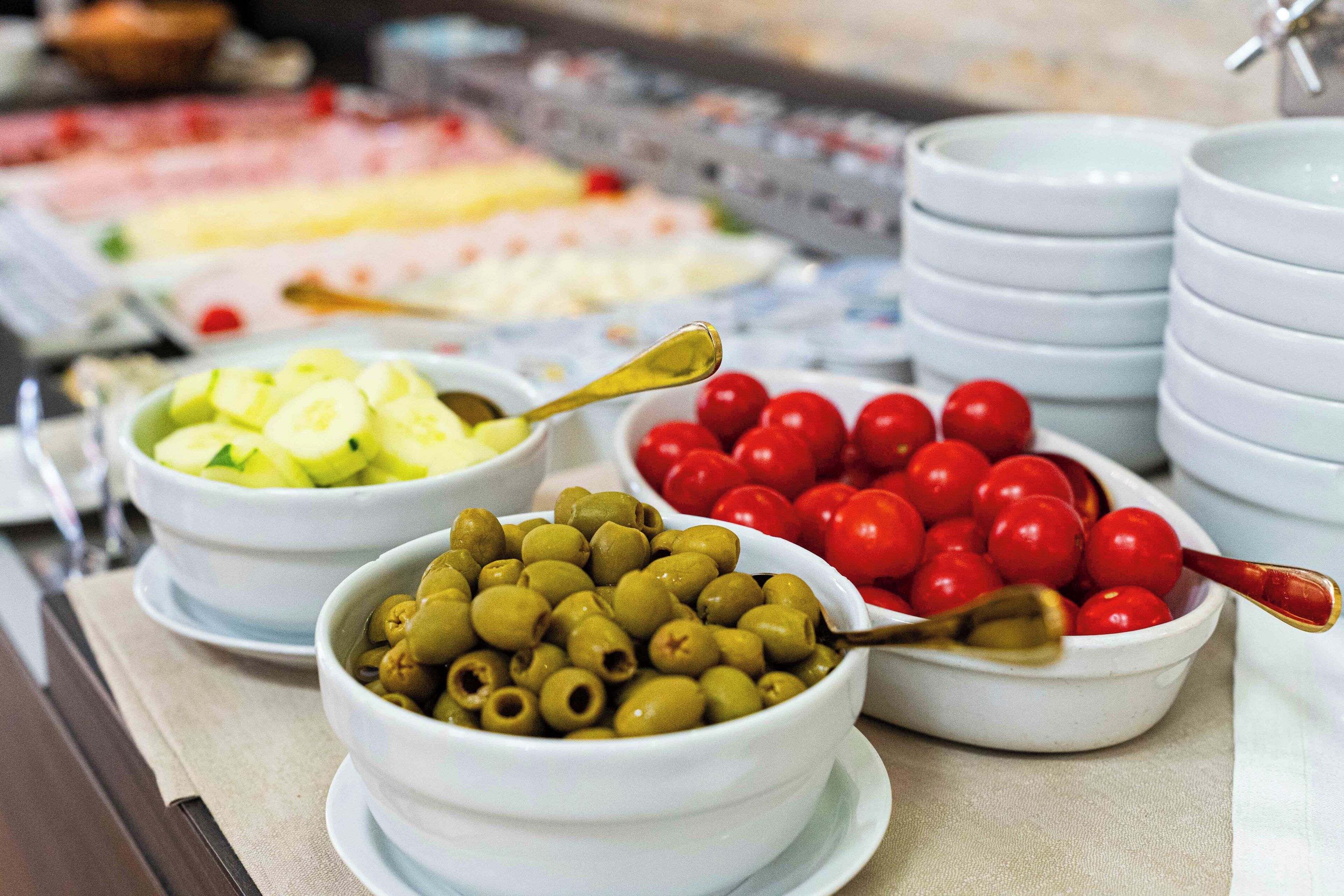 A buffet with various food items including olives, cherry tomatoes, and sliced cucumbers.