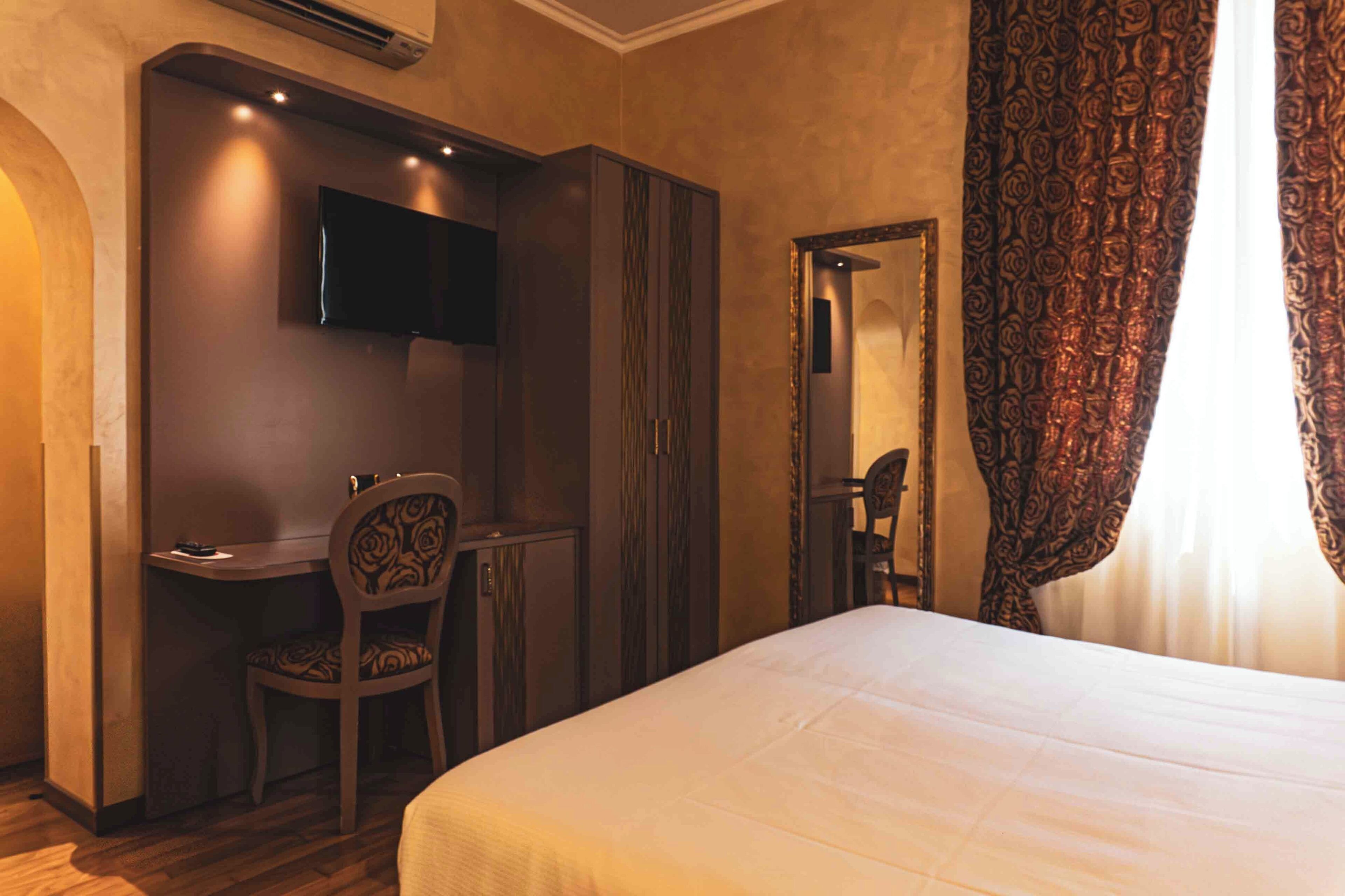 Una camera d'albergo con un letto, una scrivania, una sedia, una televisione e uno specchio.