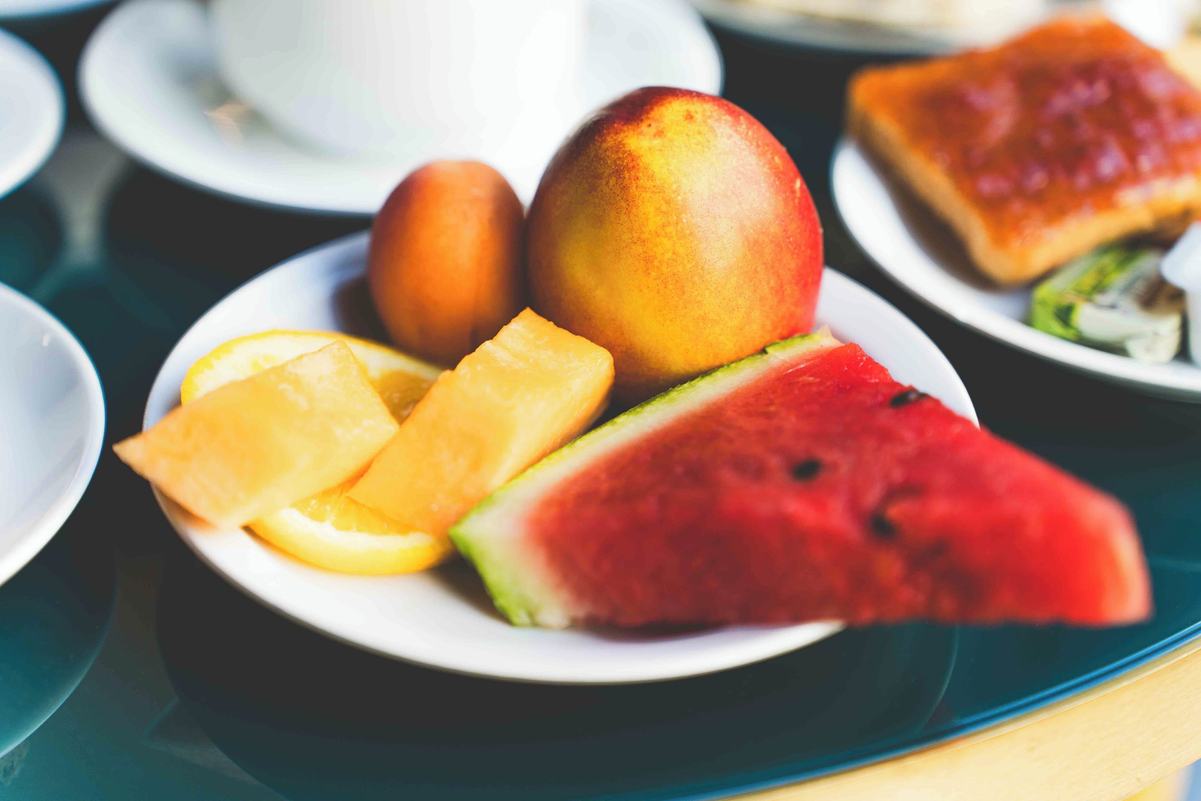 A table with a plate of fruit including watermelon, mango, and orange slices.