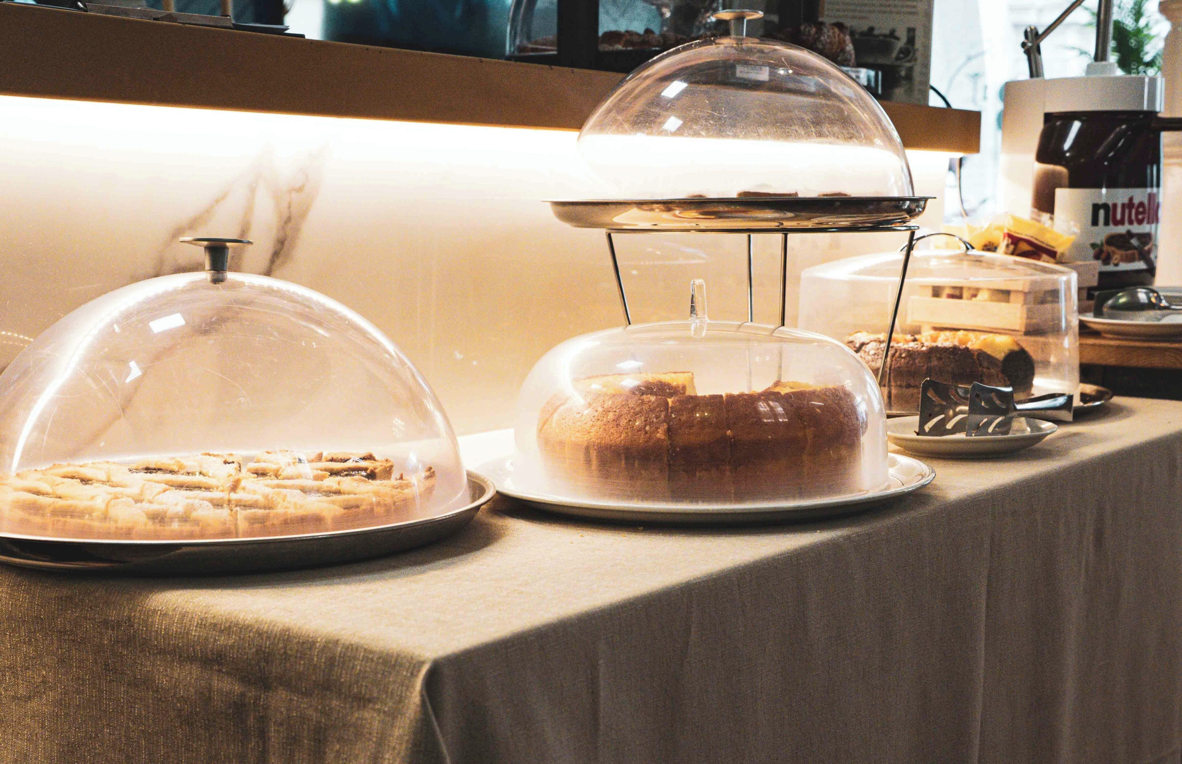 A buffet table with covered dishes, a Nutella jar, and a coffee machine.