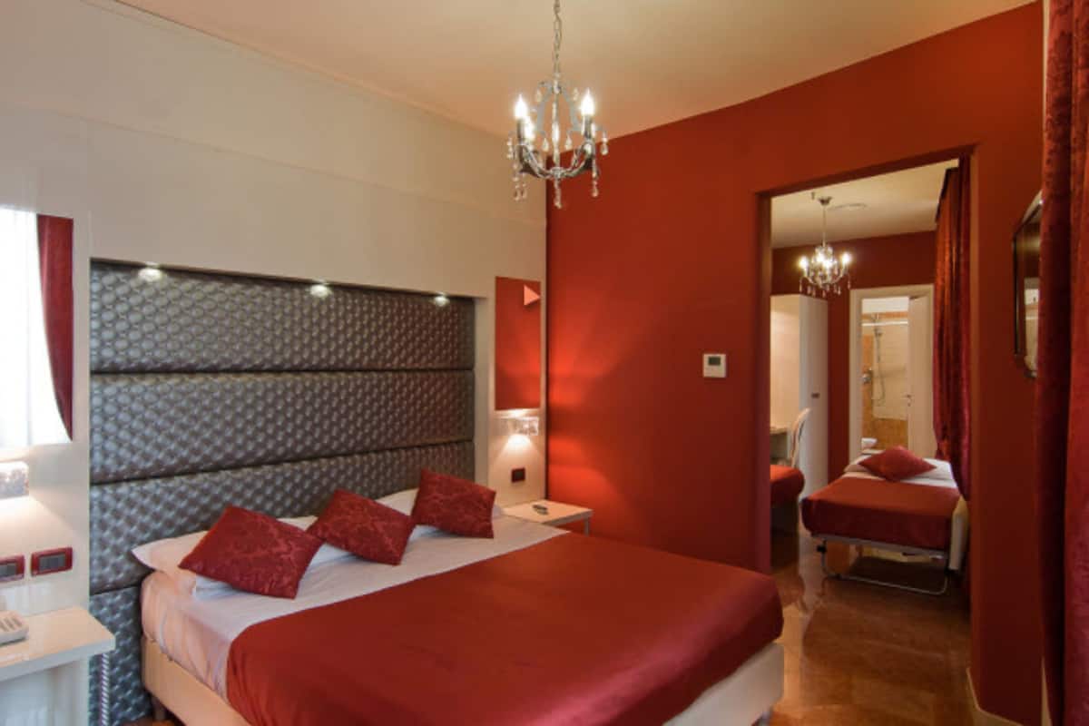 Ein Hotelzimmer mit einem großen Bett, roter Bettwäsche, einer Kristallleuchtre und einem Spiegel.