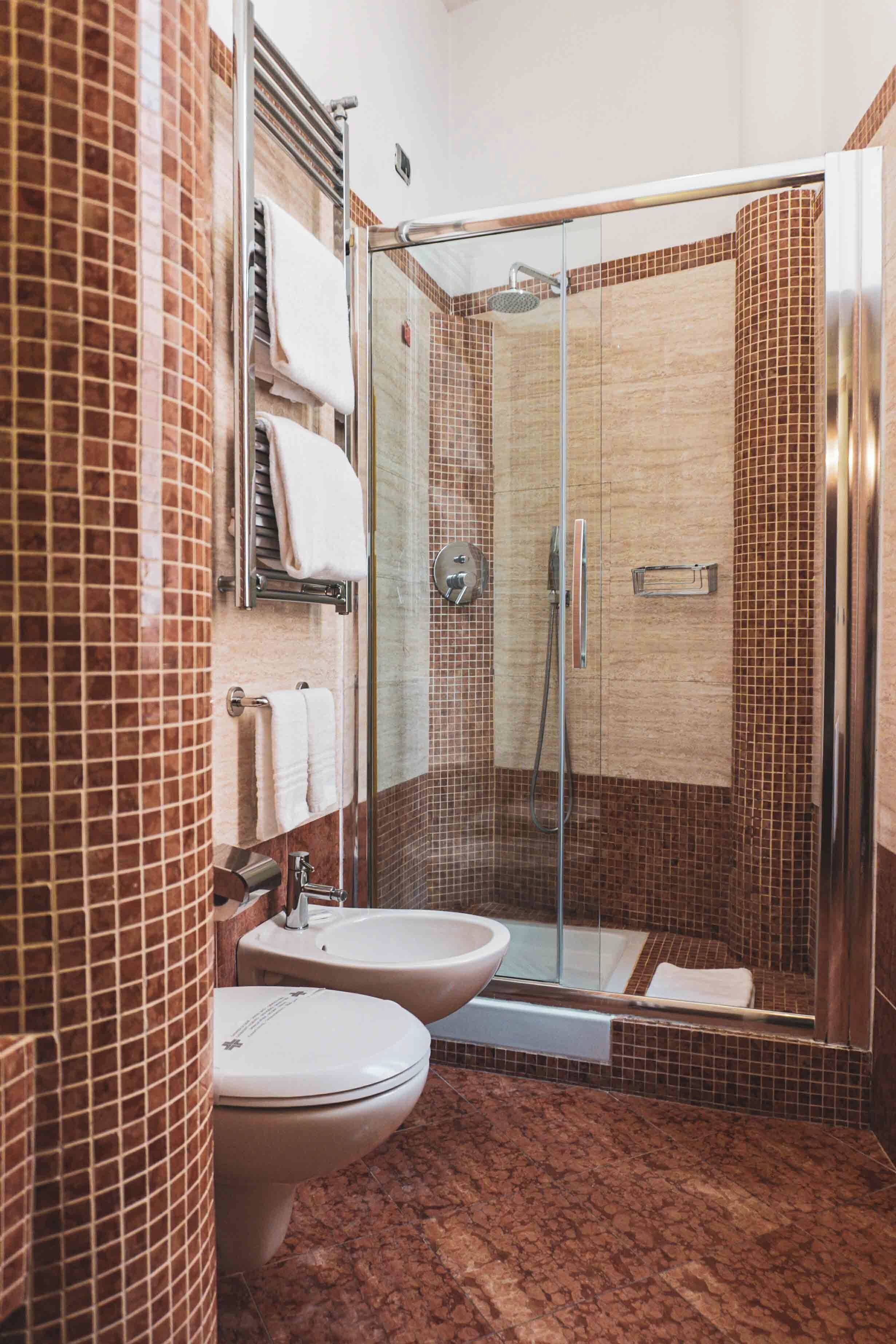 A bathroom with a glass-enclosed shower, two sinks, and a toilet.