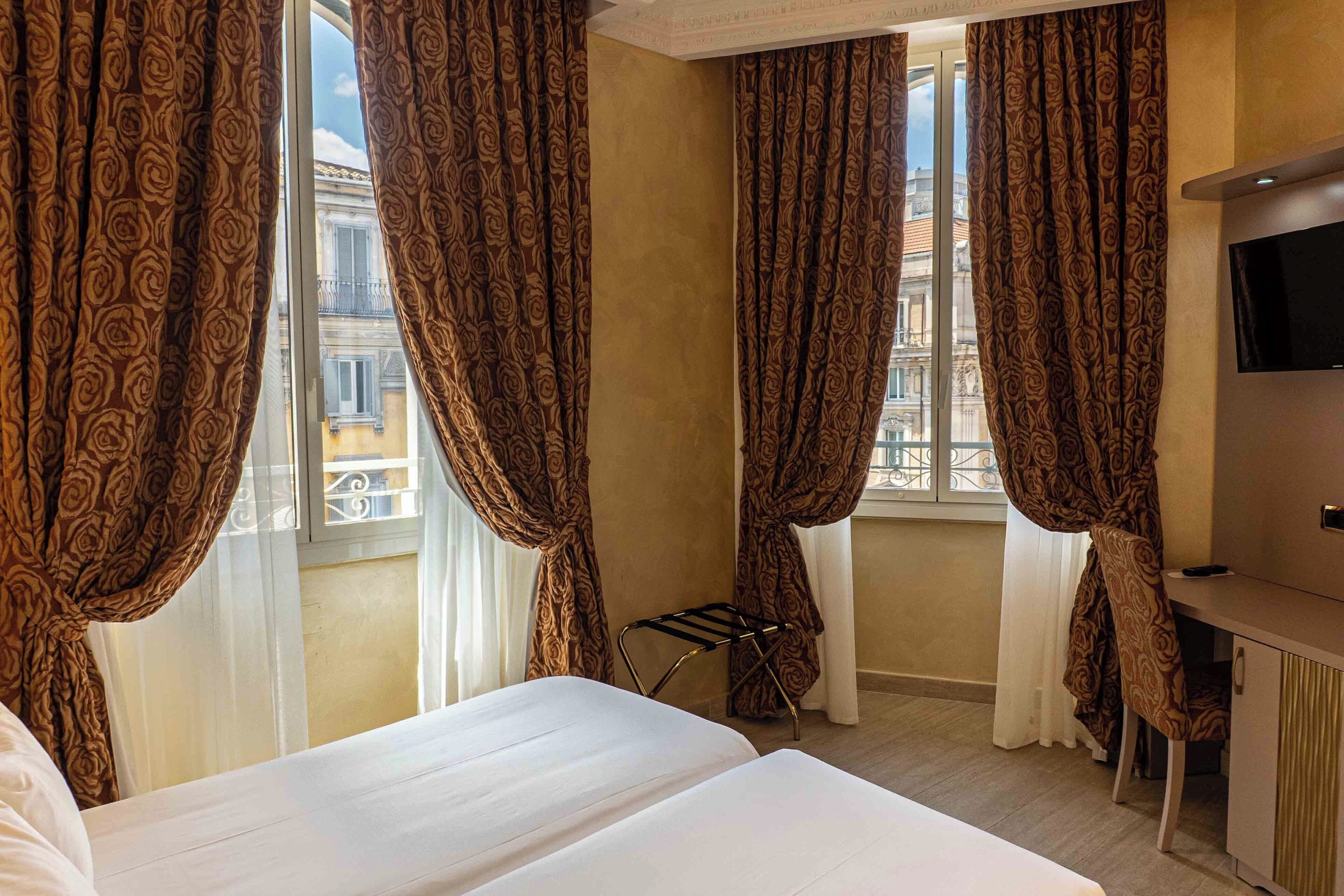 Habitación de hotel con cama, escritorio, televisor y cortinas.
