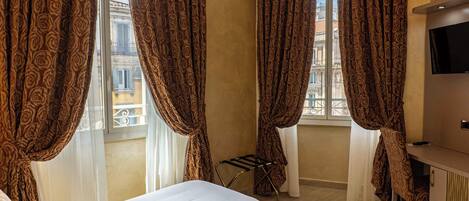 Habitación de hotel con cama, escritorio, televisor y cortinas.