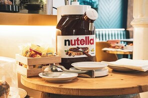 A Nutella jar on a wooden table with a spoon, a plate, and a small wooden box. - Hotel Fellini (Rome)