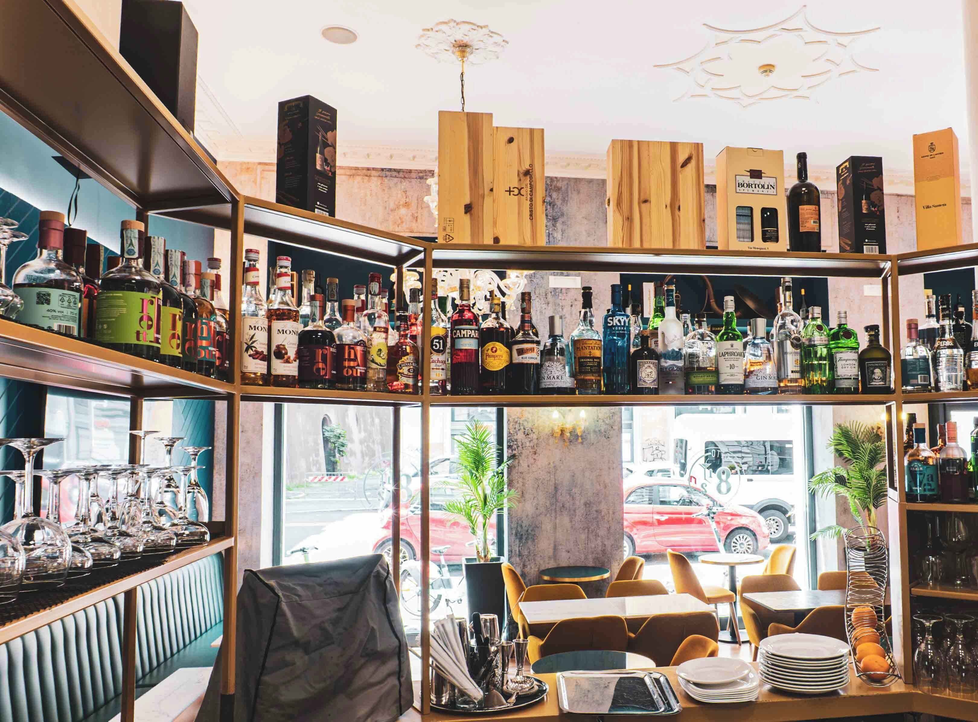 A bar area with shelves of liquor bottles, a seating area with tables and chairs, and a view of the street outside.