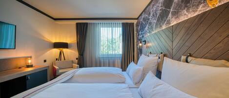 A hotel room with a large bed, a desk with a lamp, a window with curtains, and a marble accent wall.
