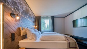 Ein modernes Hotelzimmer mit einem großen Bett, einem Holzkopfteil und Blick auf Bäume durch das Fenster.
