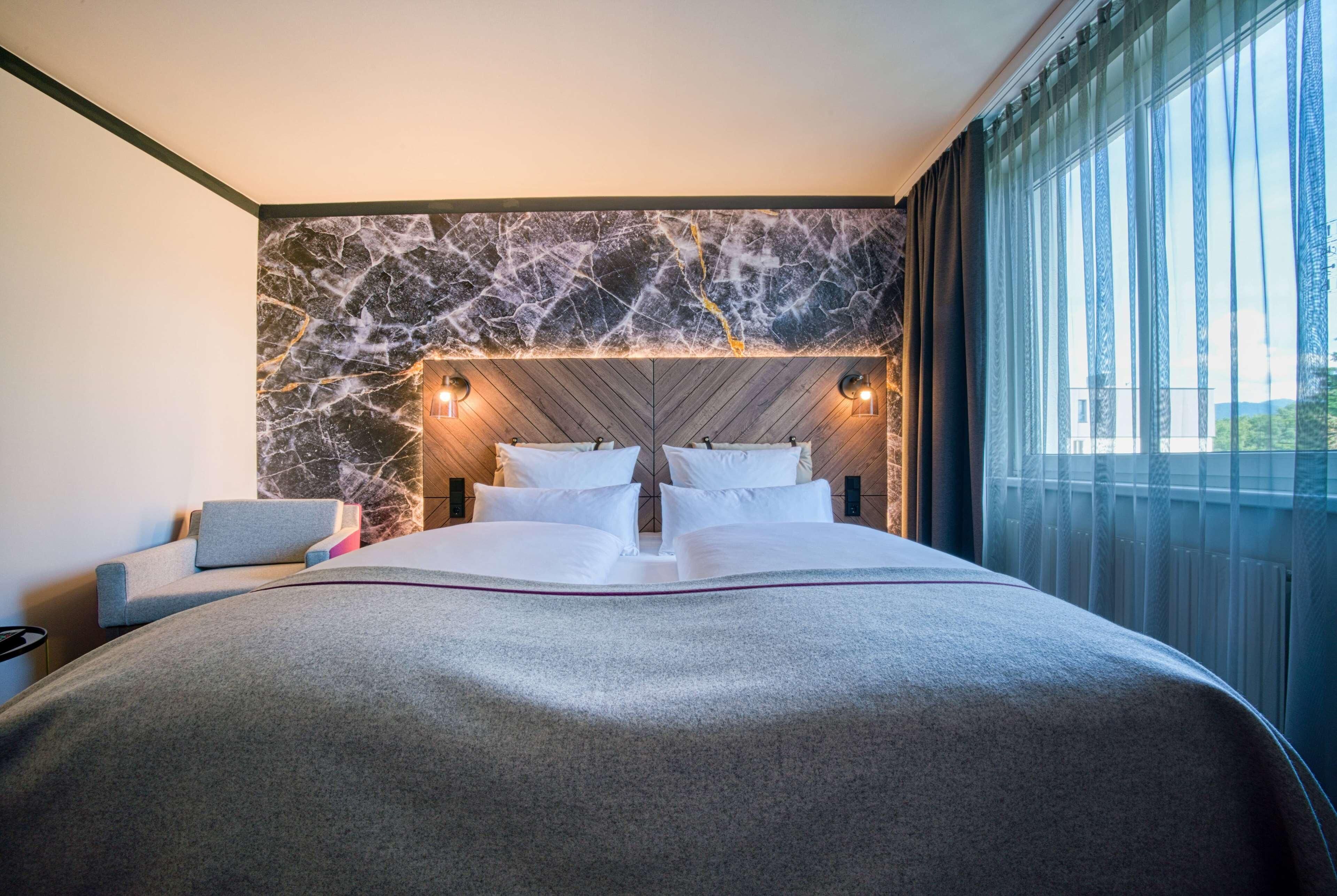 Habitación de hotel moderna con una cama grande, pared de mármol y vistas al exterior.