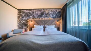 Habitación de hotel moderna con una cama grande, pared de mármol y vistas al exterior.