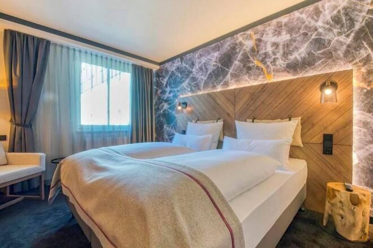 Ein Hotelzimmer mit einem großen Bett, einem Holz-Kopfteil, einem Nachttisch und einem Fenster mit Vorhängen.
