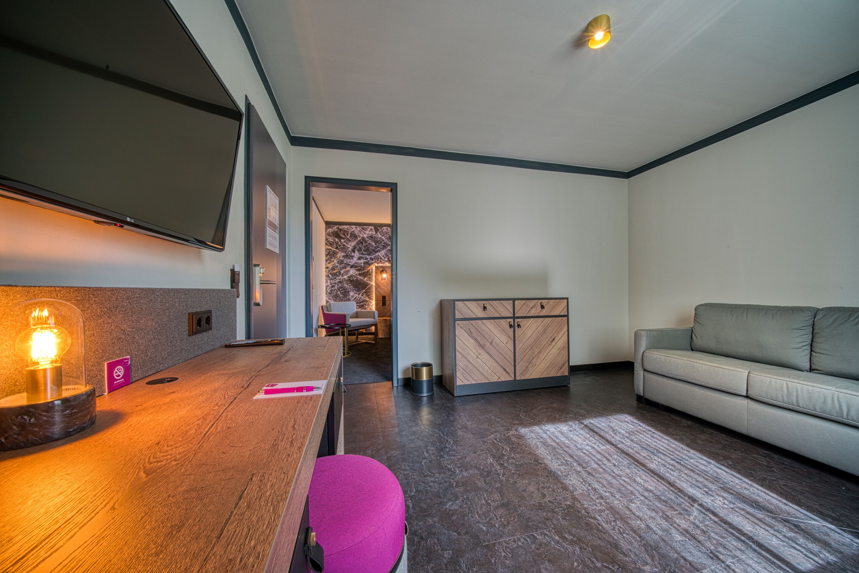A modern living room with a wooden coffee table, a pink ottoman, a grey sofa, and a cabinet.