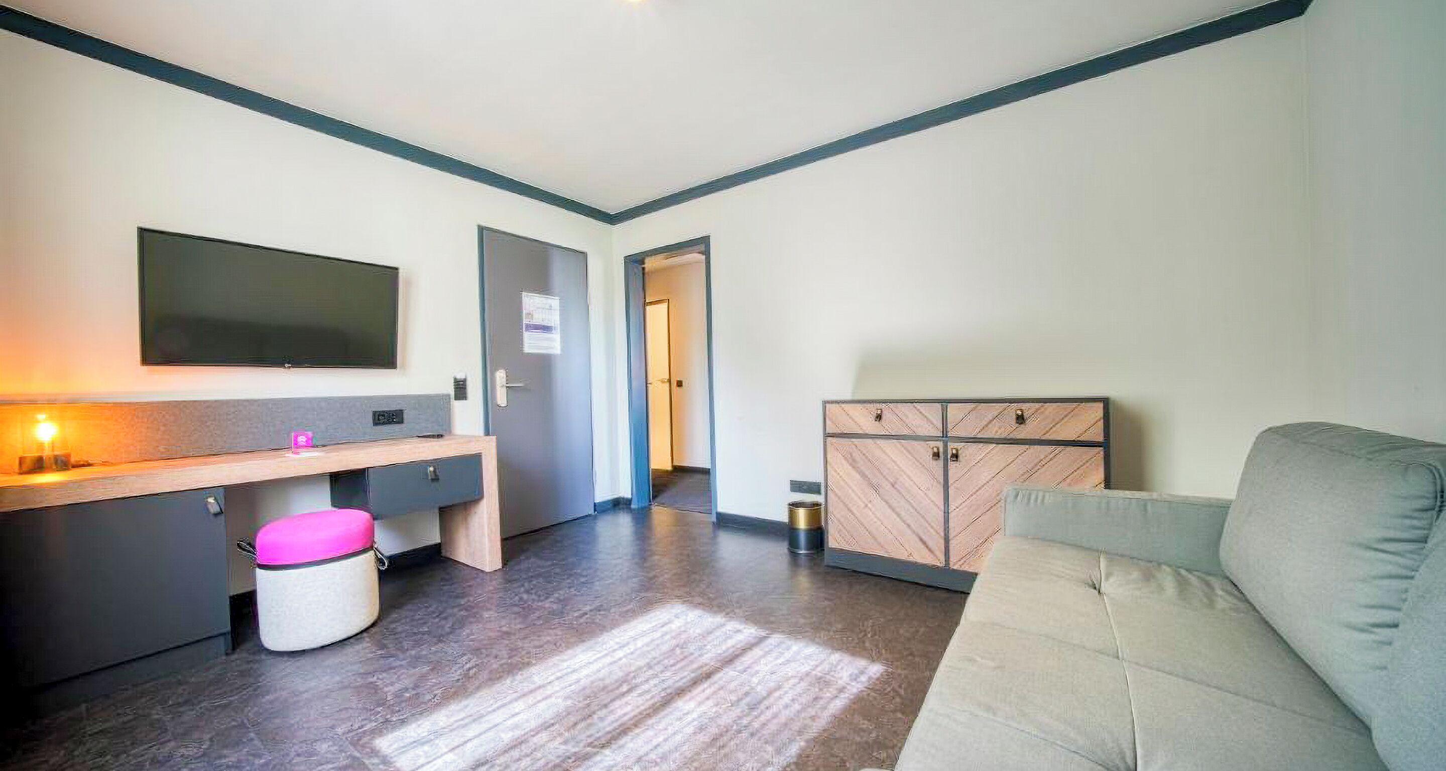 Una sala de estar moderna con un sofá, un televisor de pantalla plana, un mueble de madera y un taburete pequeño.