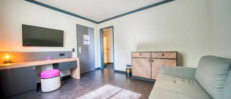 Una sala de estar moderna con un sofá, un televisor de pantalla plana, un mueble de madera y un taburete pequeño.
