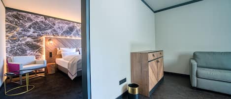 Una habitación de hotel moderna con una pared de acento de mármol, una cama, una mesita, un sofá y un armario de madera.
