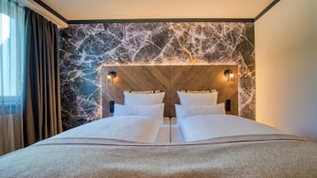 Habitación de hotel con una cama grande, cabecero de madera, pared de mármol y dos luces fijadas a la pared.