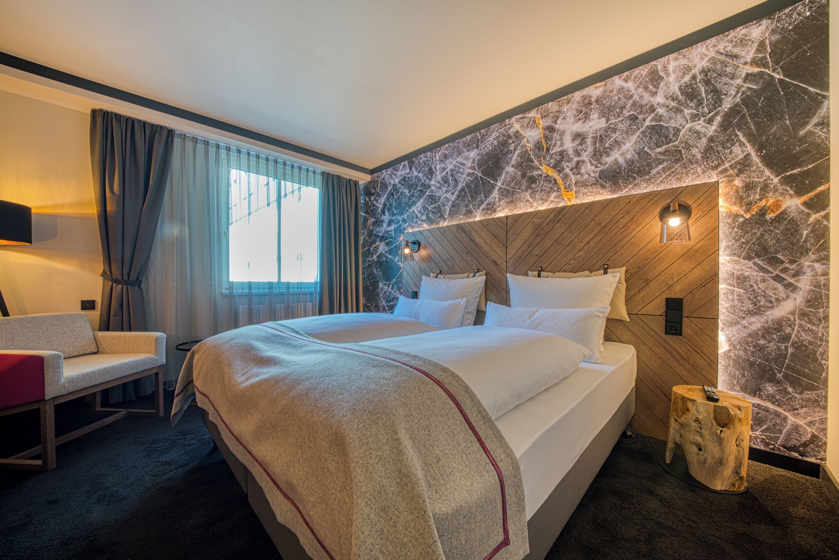 Una habitación de hotel con una cama grande, un escritorio, una silla, un cabecero de madera y una pared de mármol.