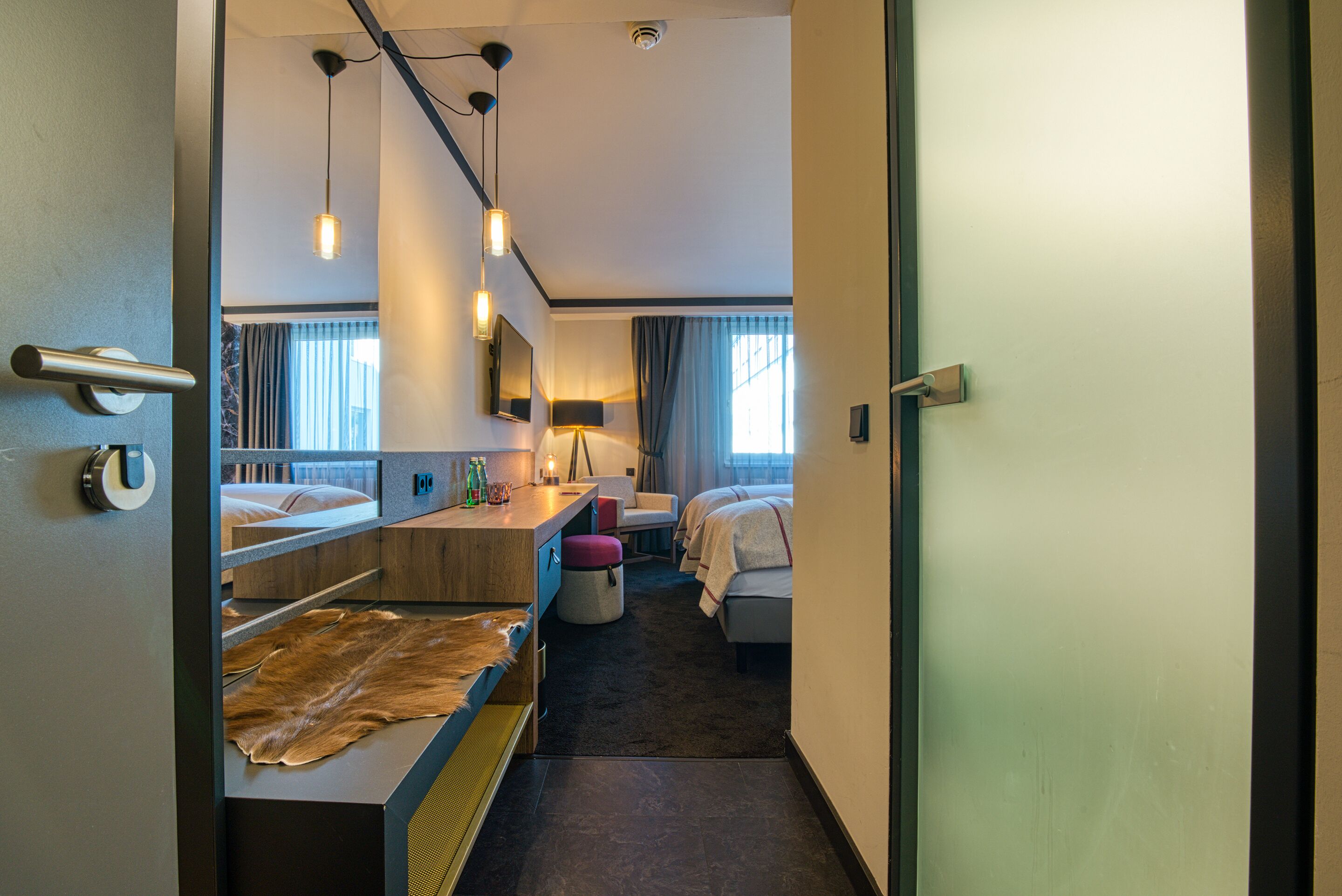 A hotel room with a bed, a desk, a chair, a lamp, and a large mirror.