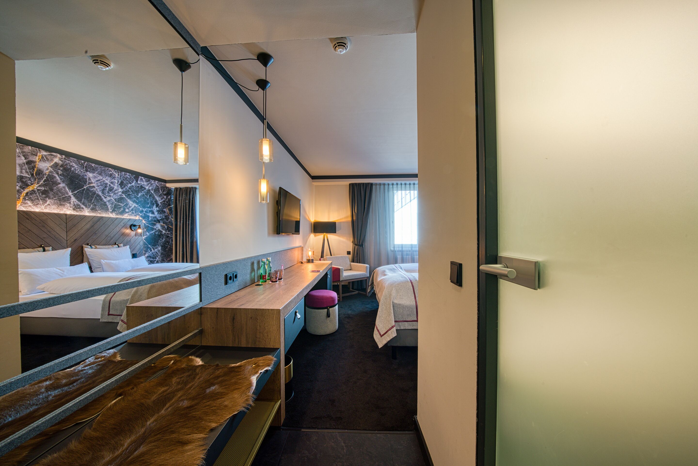 Una habitación de hotel moderna con cama, escritorio, silla y un espejo grande.