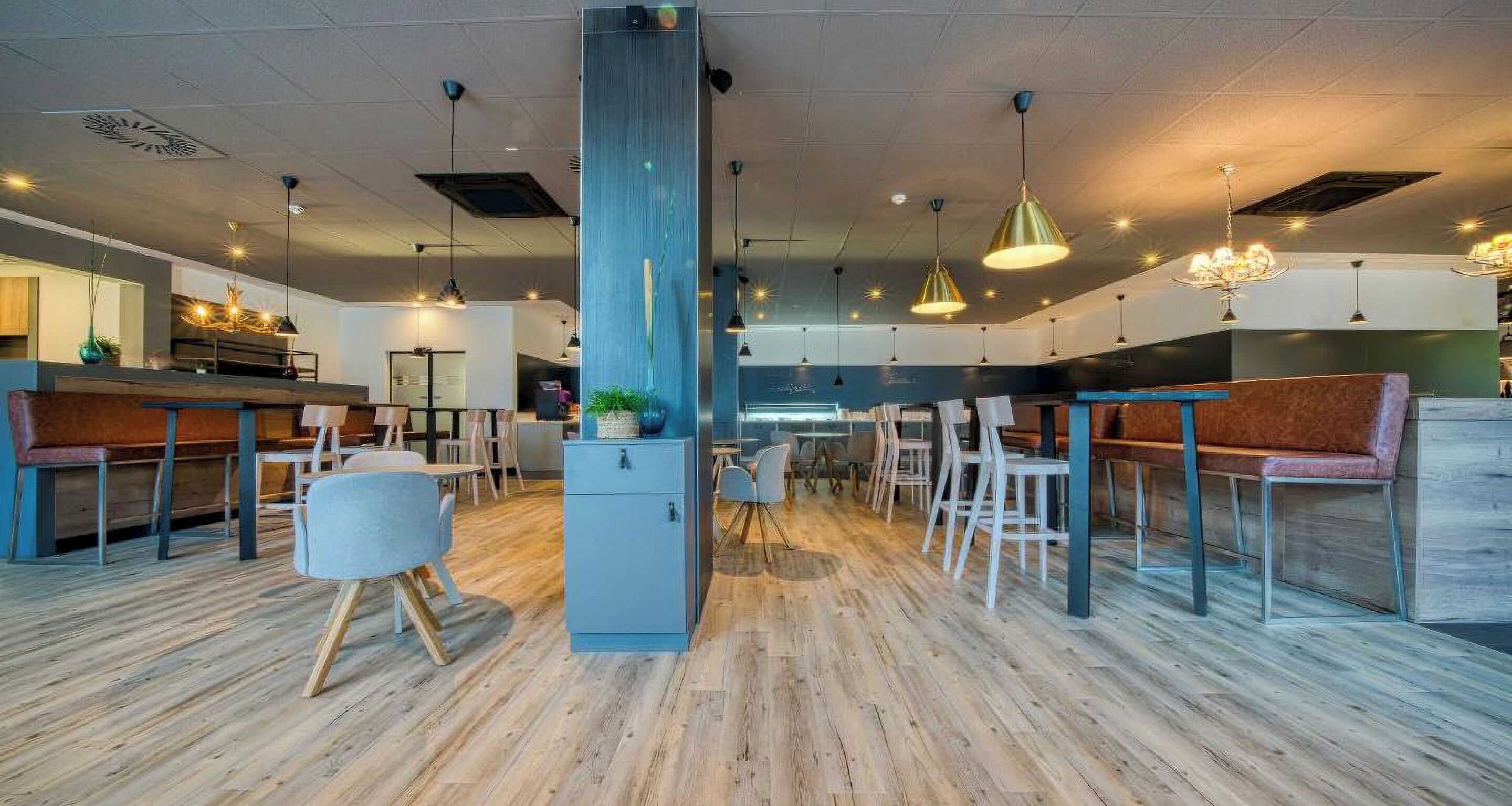 Un interior moderno con piso de madera, asientos de bar e iluminación colgante.
