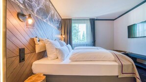 A hotel room with a bed, wall-mounted light fixtures, a flat-screen TV, and a window with curtains. - PLAZA INN Salzburg Messe  (Salzburg)