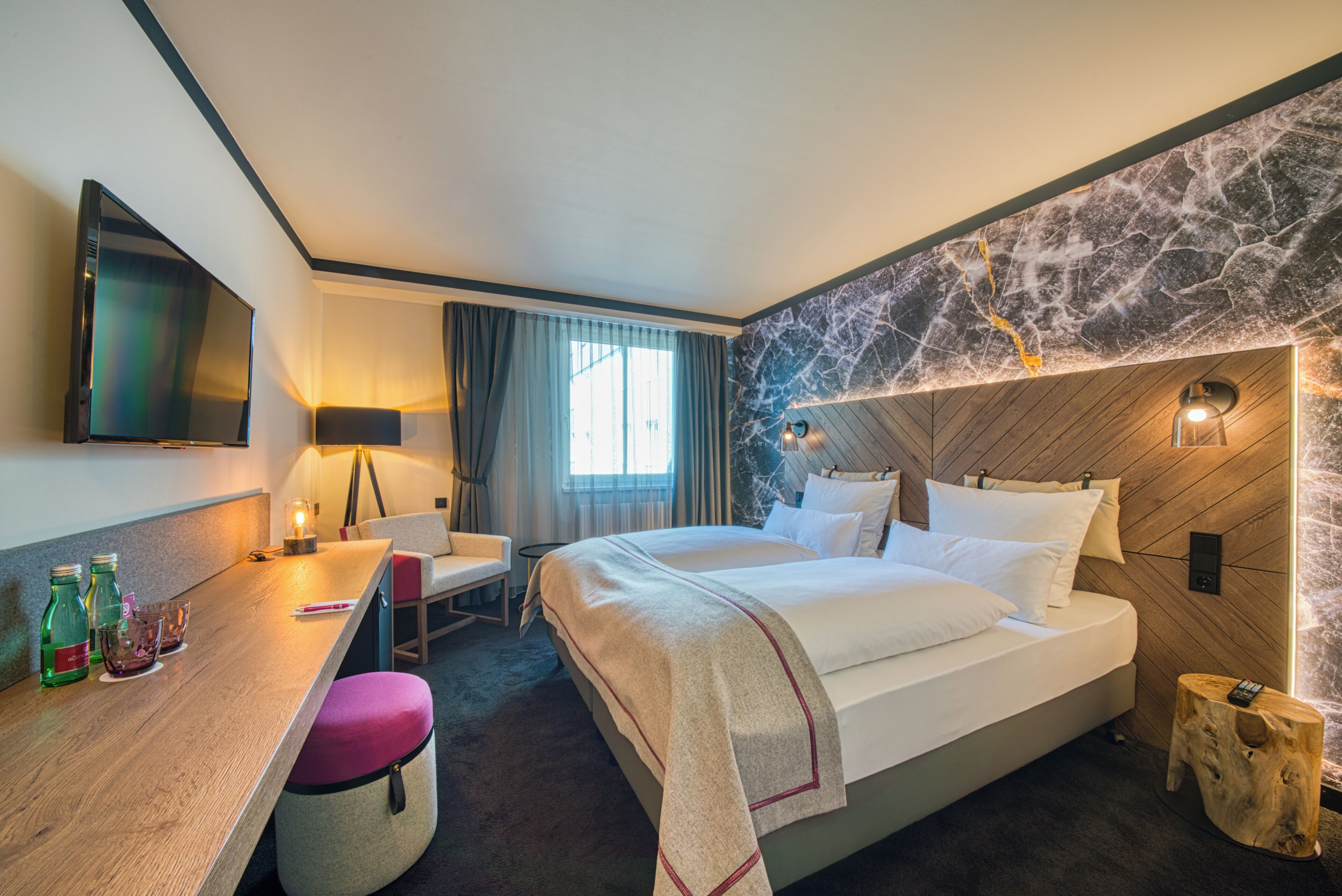 A hotel room with a bed, a desk, a chair, a TV, and a window with curtains.