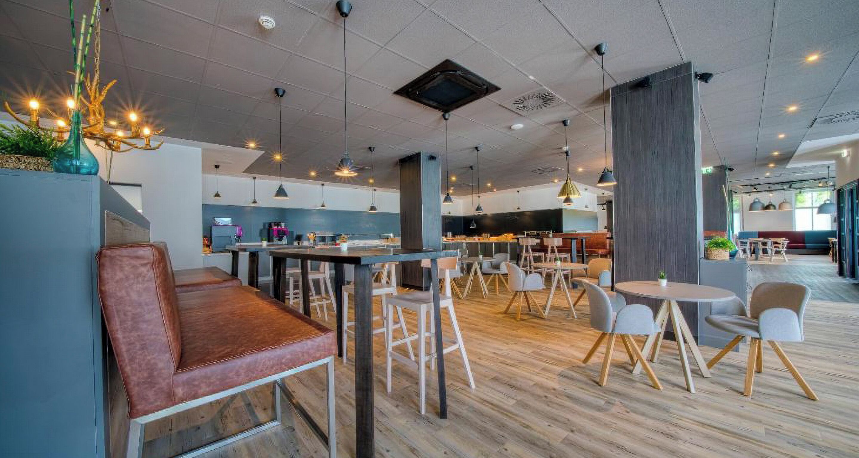 Un restaurante moderno con suelo de madera, varias zonas de estar, iluminación colgante y una barra.