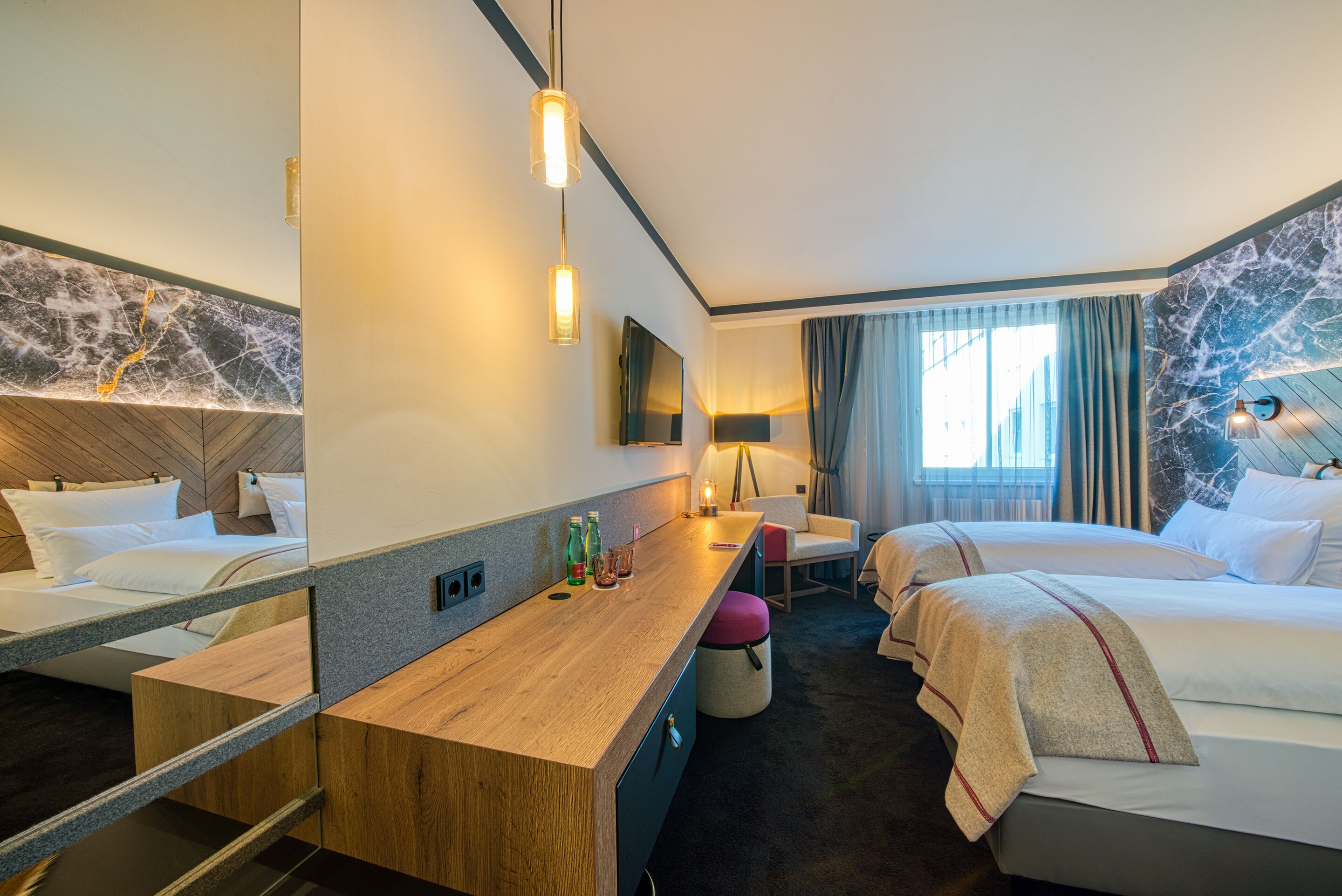 Een hotelkamer met een houten bureau, twee bedden, een televisie en een grote spiegel.