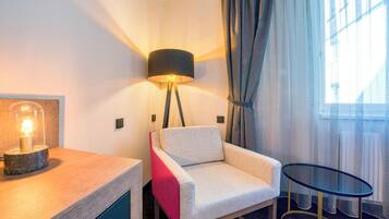 Une chambre d’hôtel avec une lampe moderne, une chaise, une petite table et une vue sur l’extérieur à travers des rideaux transparents.