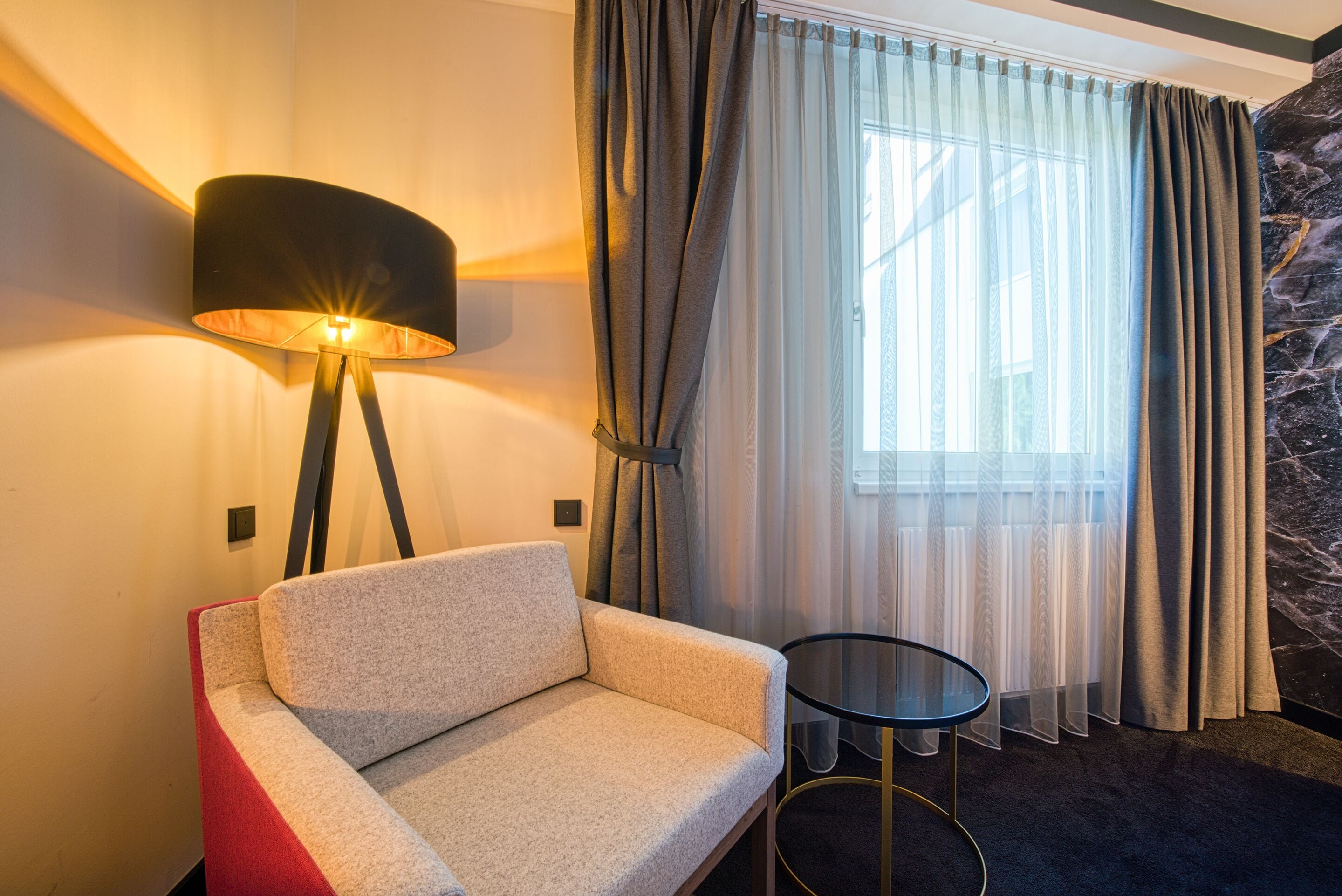 Una habitación de hotel moderna con sofá, una mesita redonda y una lámpara de pie.