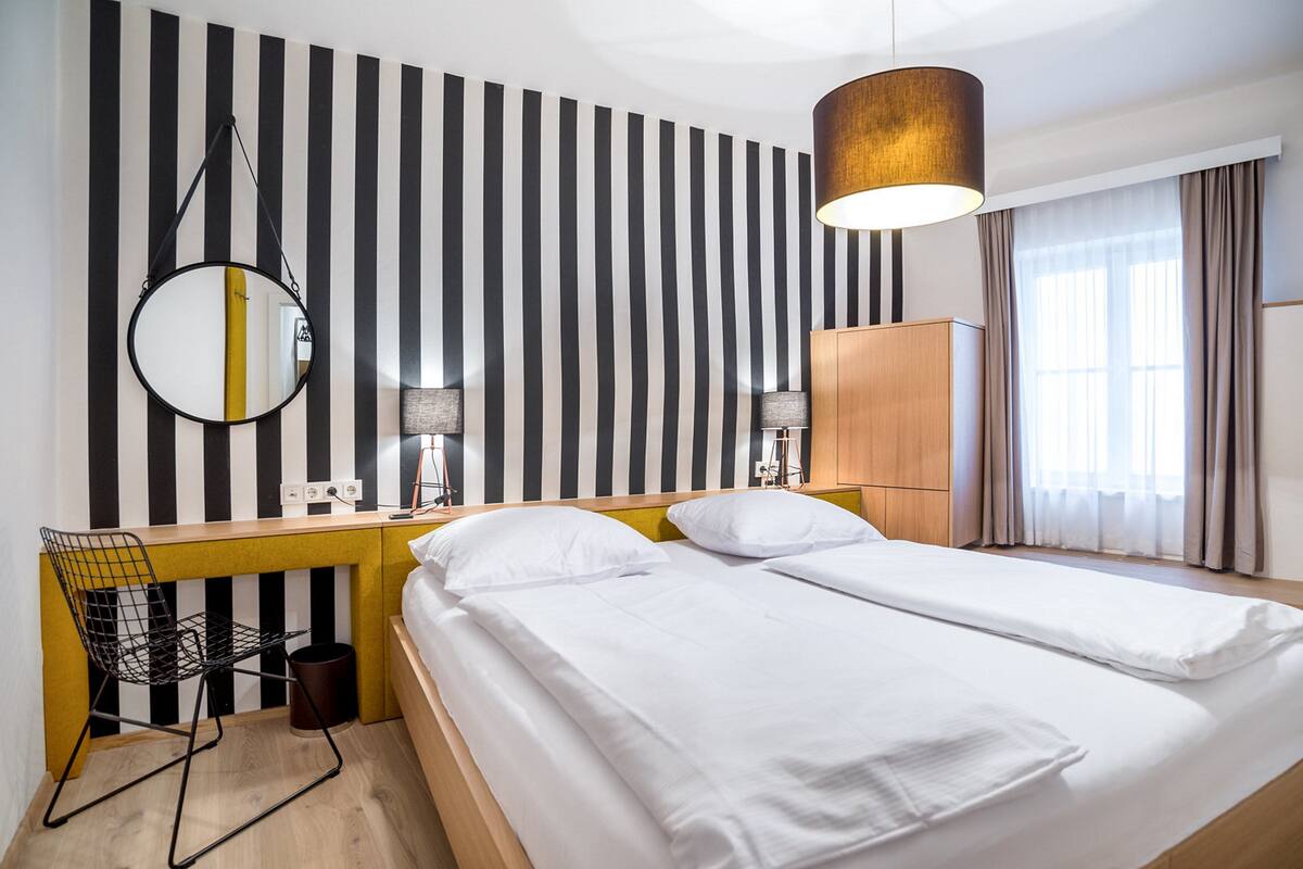 Habitació d'hotel amb un llit, un escriptori amb cadira, un mirall i un armari.