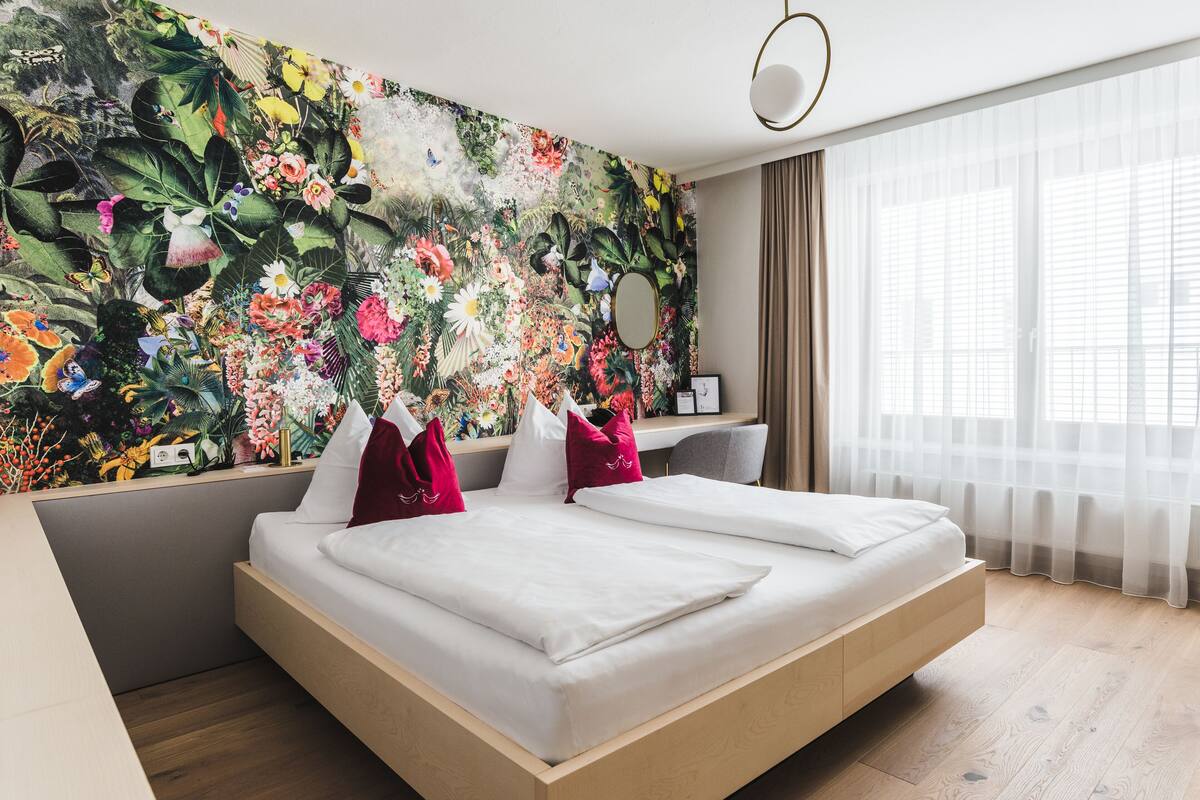 Habitació d'hotel moderna amb un llit gran, un escriptori i un mural floral colorit a la paret.