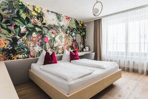 Una habitación de hotel moderna con una cama grande, un escritorio y un mural floral llamativo en la pared.