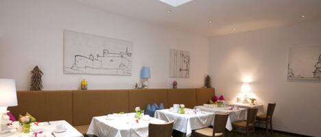A dining area with tables set for meals, a bench, and artwork on the walls.