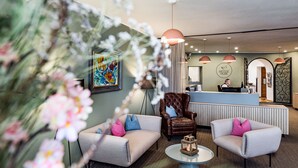 A reception area with a reception desk, two armchairs, a coffee table, and a large painting on the wall.
