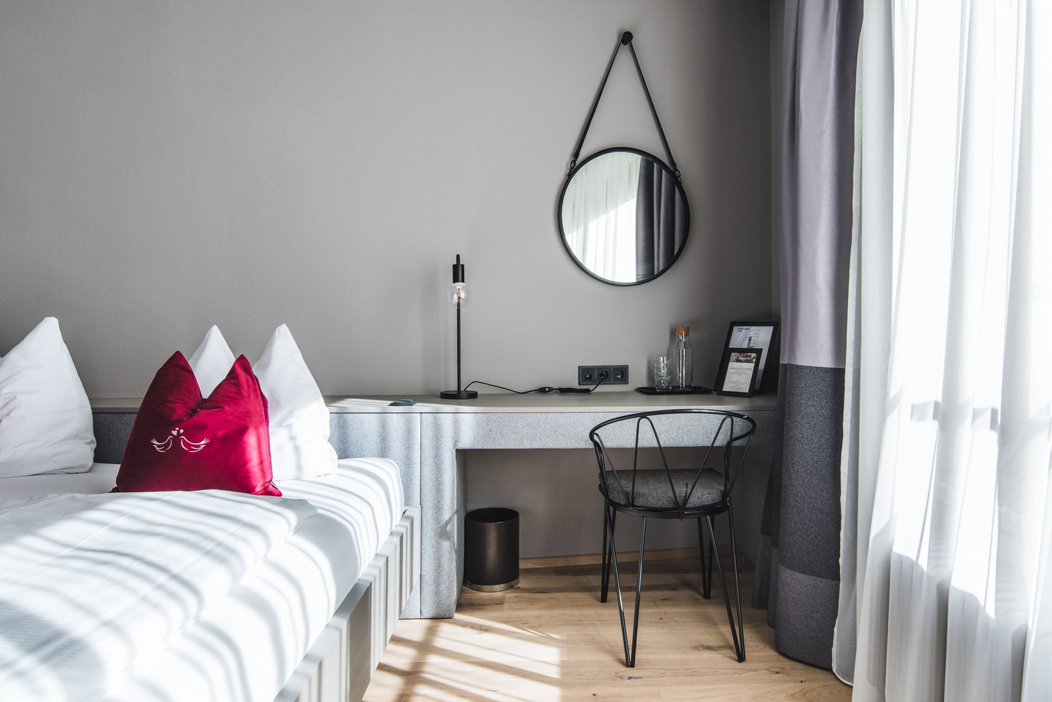 Une chambre moderne comprenant un lit, une table de chevet, un bureau, une chaise et un miroir suspendu.