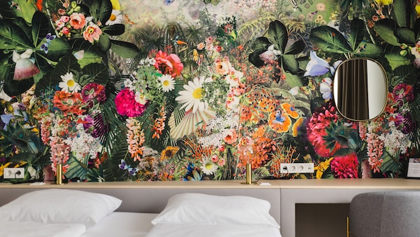 A bedroom with a floral wallpaper, a bedside table, a mirror, and a bed.