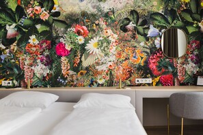 Un dormitorio con papel tapiz floral, una mesita de noche, un espejo y una cama.