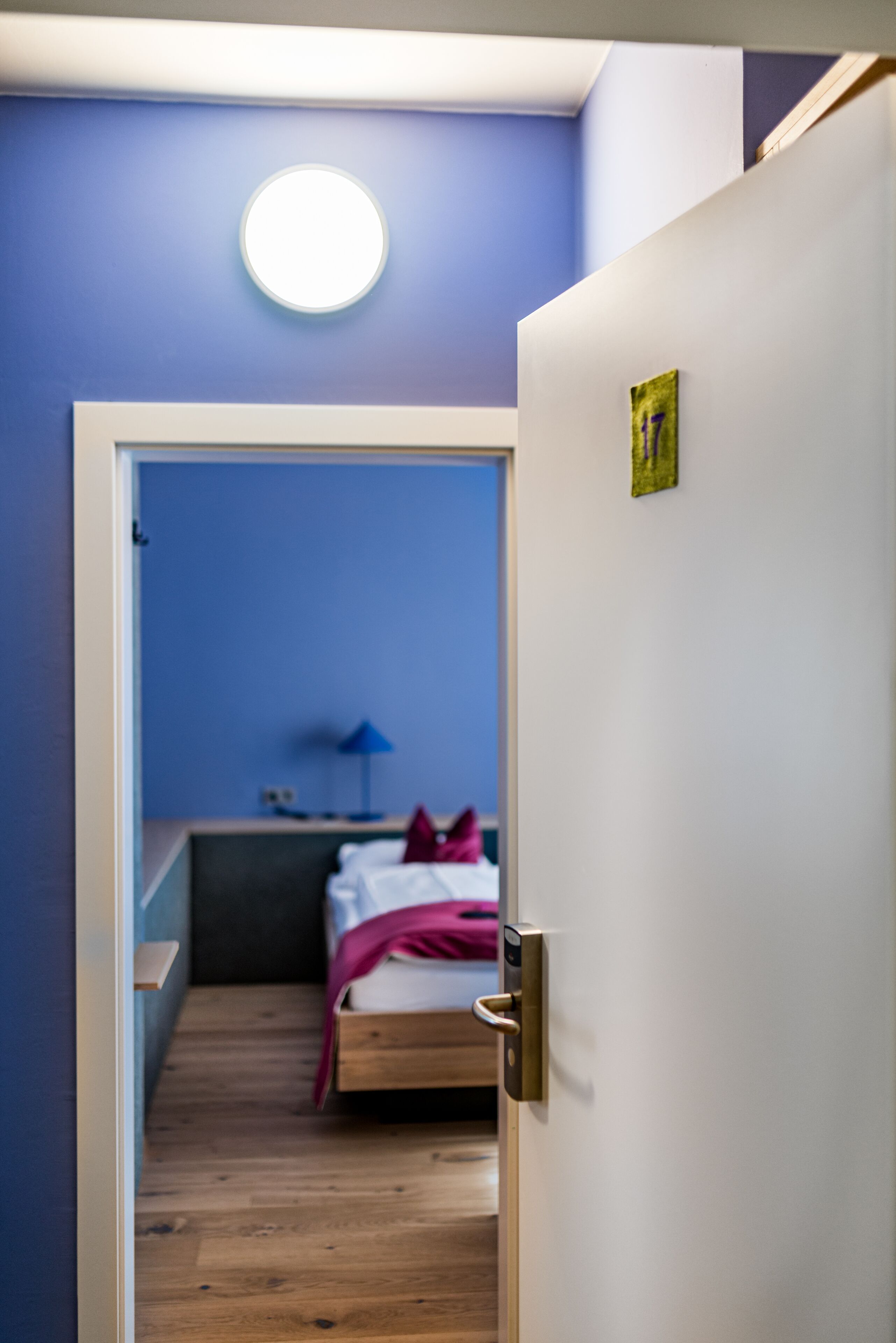A narrow hallway leading to a bedroom with a bed, a nightstand, and a lamp.