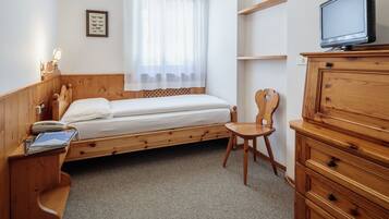 Een slaapkamer met een houten bed, een nachtkastje met lamp, een stoel, een houten dressoir en een televisie bovenop het dressoir.
