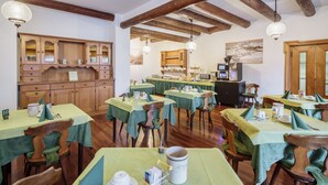 Zona de dinar amb diverses taules cobertes amb mantells verds, cadires de fusta i un armari de fusta amb portes de vidre.