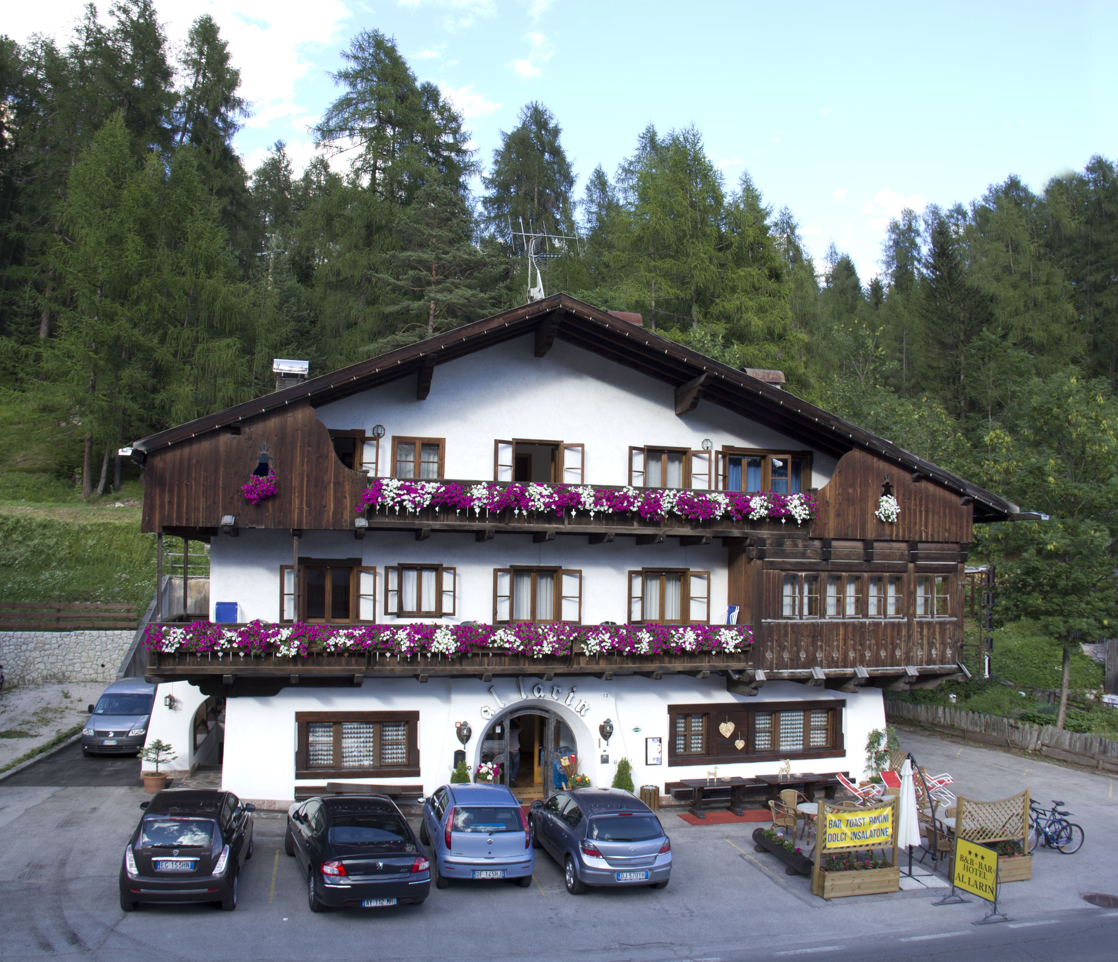 Ein zweistöckiges Gebäude mit einem Blumen-geschmückten Balkon, einem Parkplatz mit Autos und einem Schild für ein Restaurant.