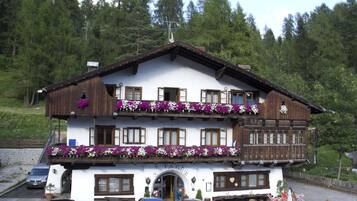 Un immeuble de deux étages doté d’un balcon orné de fleurs, une aire de stationnement avec des voitures et une enseigne indiquant un restaurant.