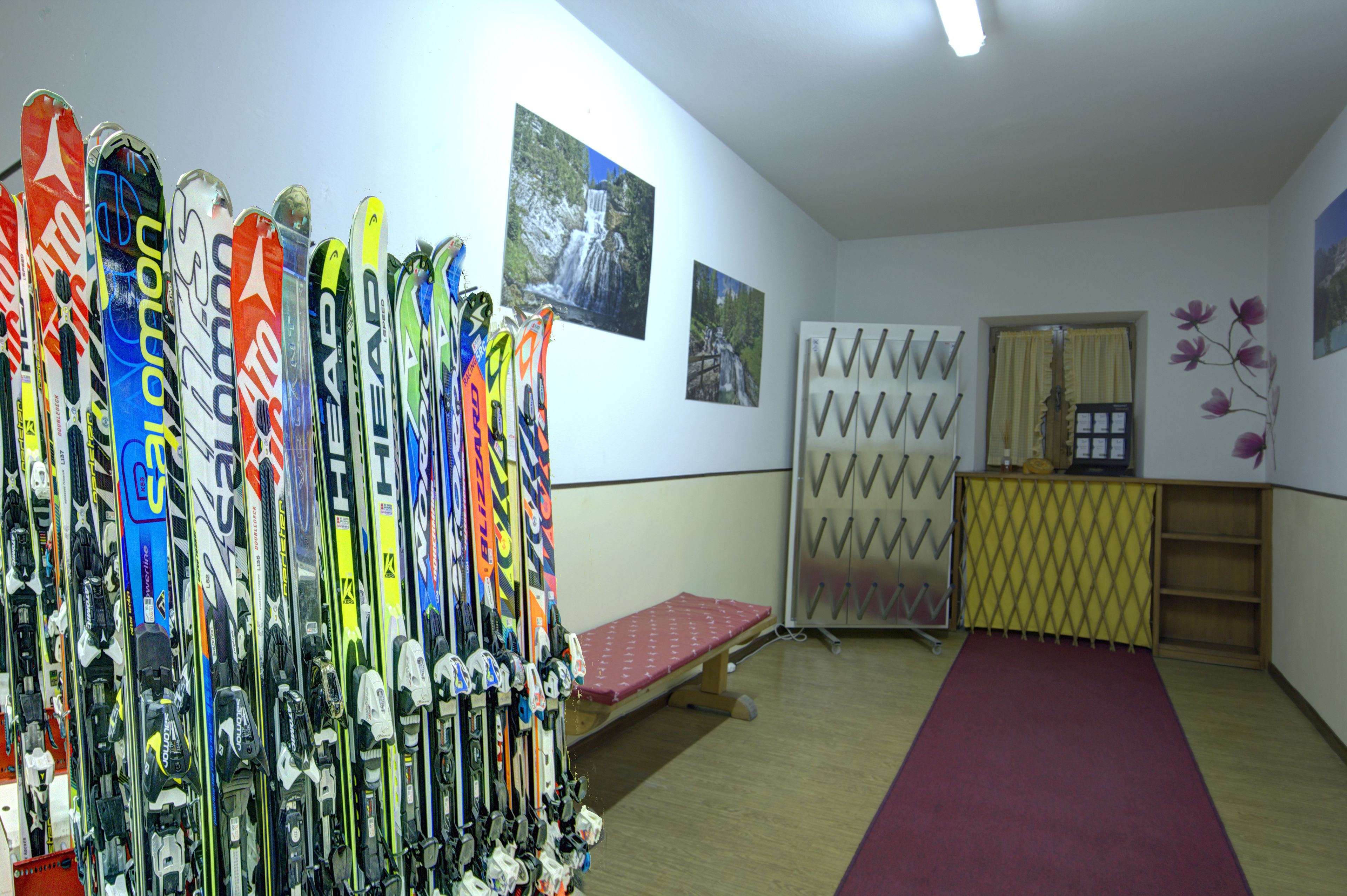 Una sala de alquiler de esquíes con esquíes y tablas de snowboard en estantes, un banco y un mostrador de recepción.