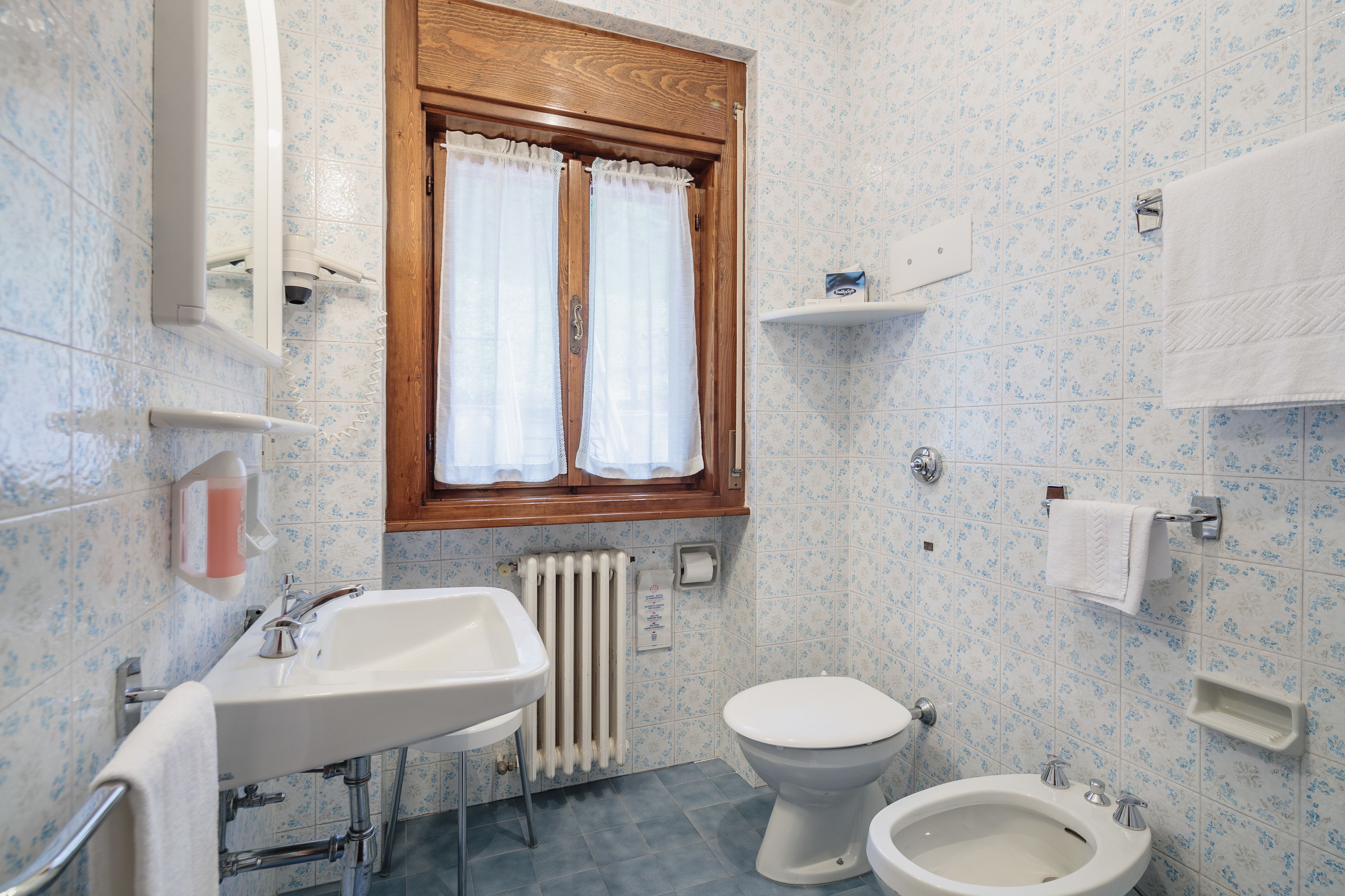 Een badkamer met een wastafel, toilet, bidet en een raam met gordijnen.